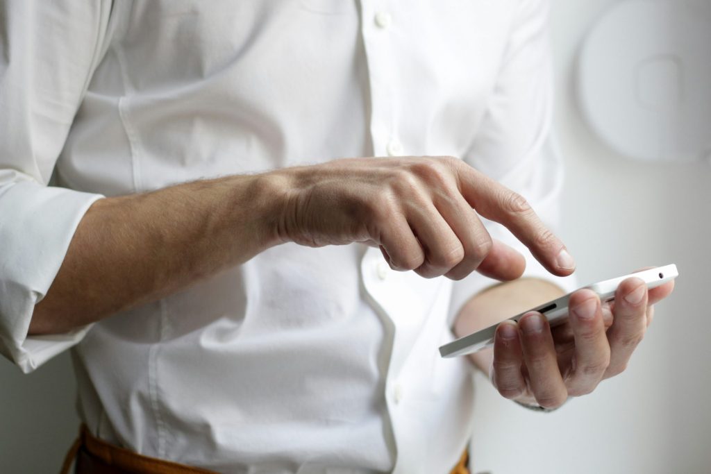 personne tenant un smartphone Android blanc et portant une chemise blanche